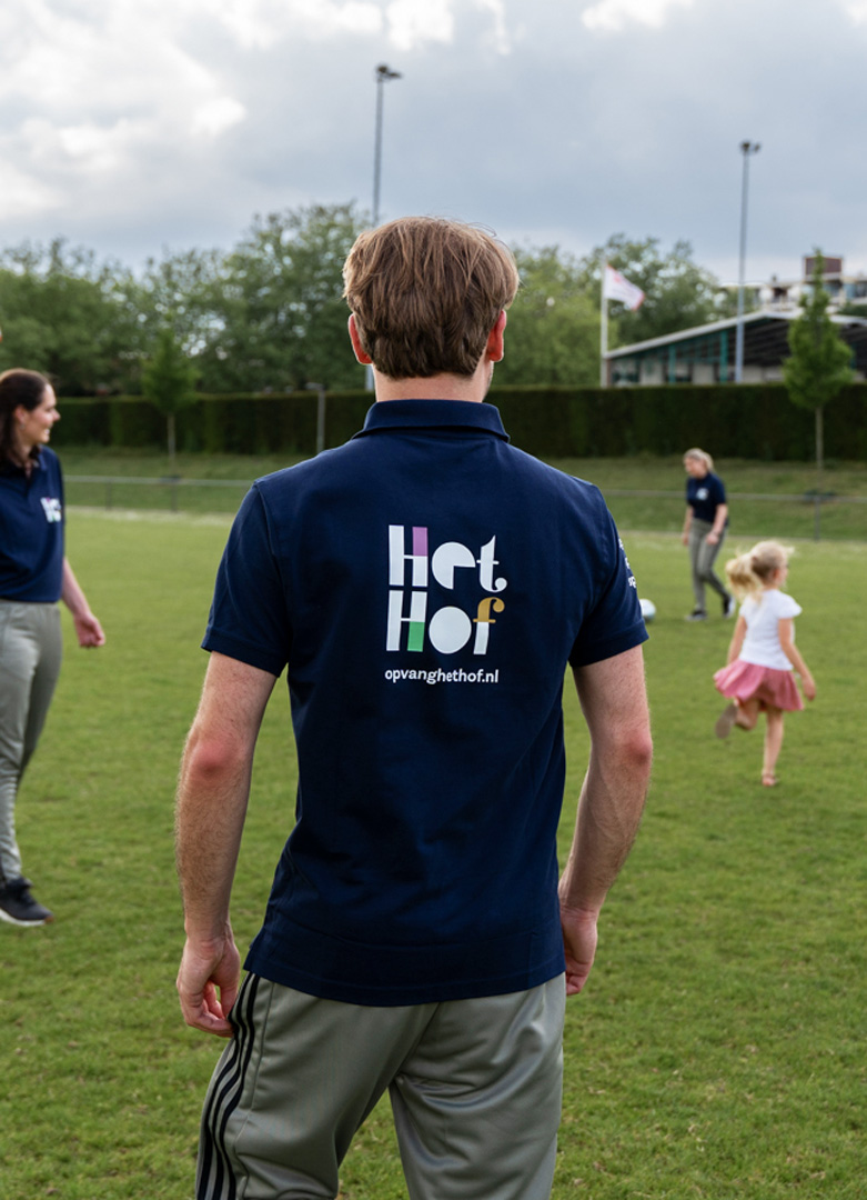 Logo ontwerp op rug van T-shirt afgebeeld, jongen staat op sportveld met kinderen